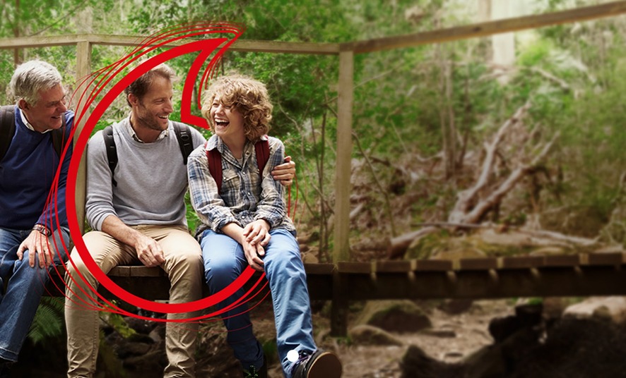 A family seated on a wooden bridge, surrounded by lush greenery in a serene forest setting.